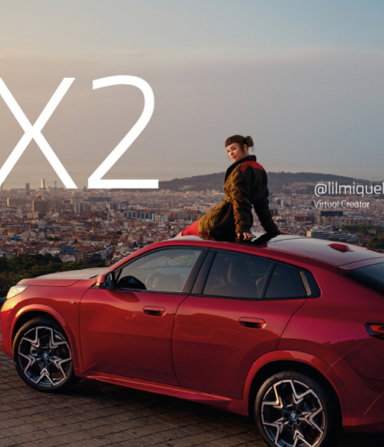 BMW The new iX2 car in red seen from the back. Lil Miquela is sitting on top of the roof of the car. The car looks out on the city below.