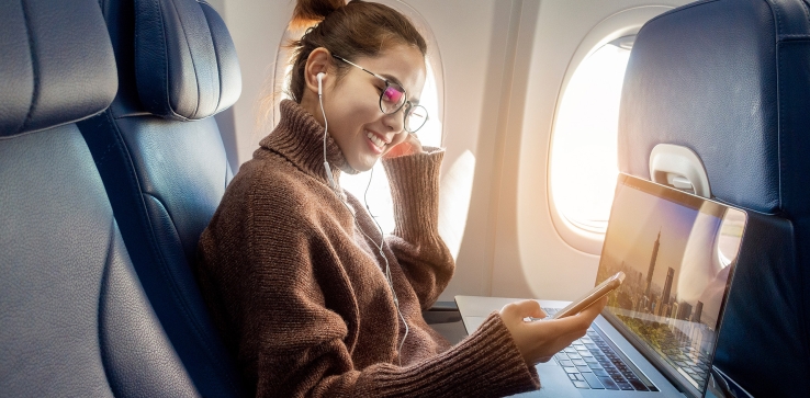 A person on an airplane using their cellphone and laptop
