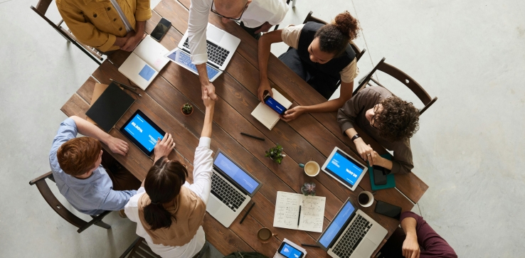 Table seen from above with people sitting around it and two people are shaking hands
